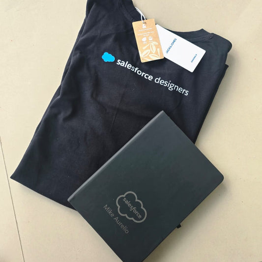 Black t-shirt and black notebook with Salesforce logo on a light beige surface